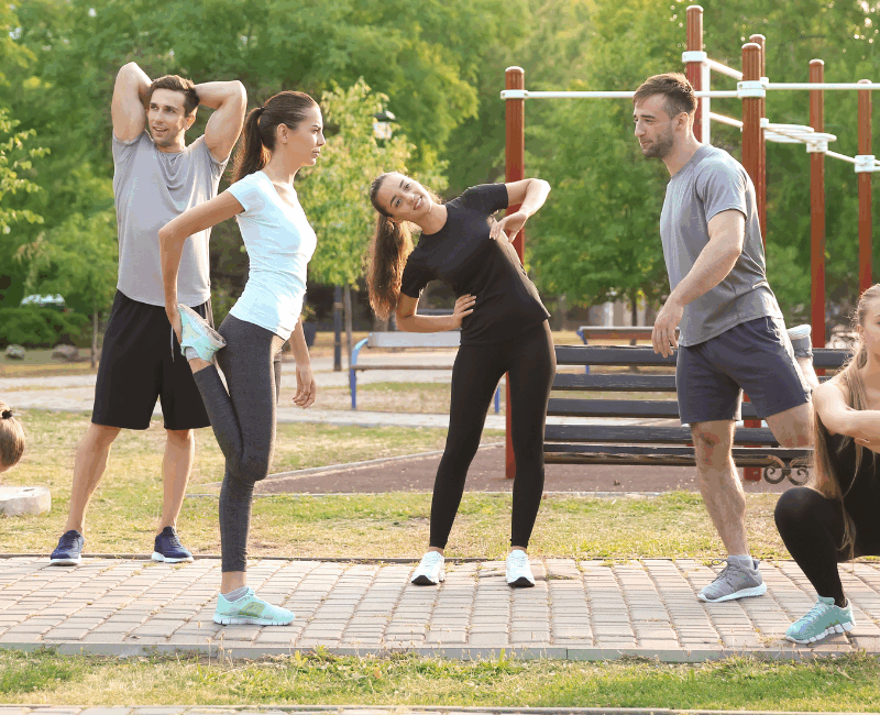 Grupa osób wykonujących rozgrzewkę na świeżym powietrzu w parku latem