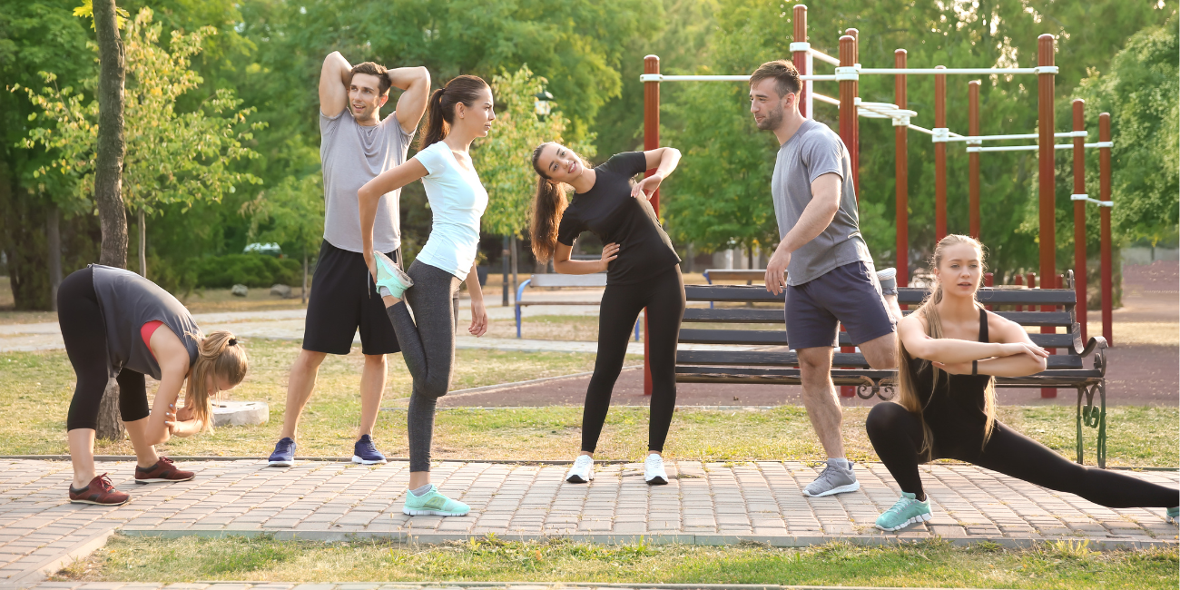 Grupa osób wykonujących rozgrzewkę na świeżym powietrzu w parku latem
