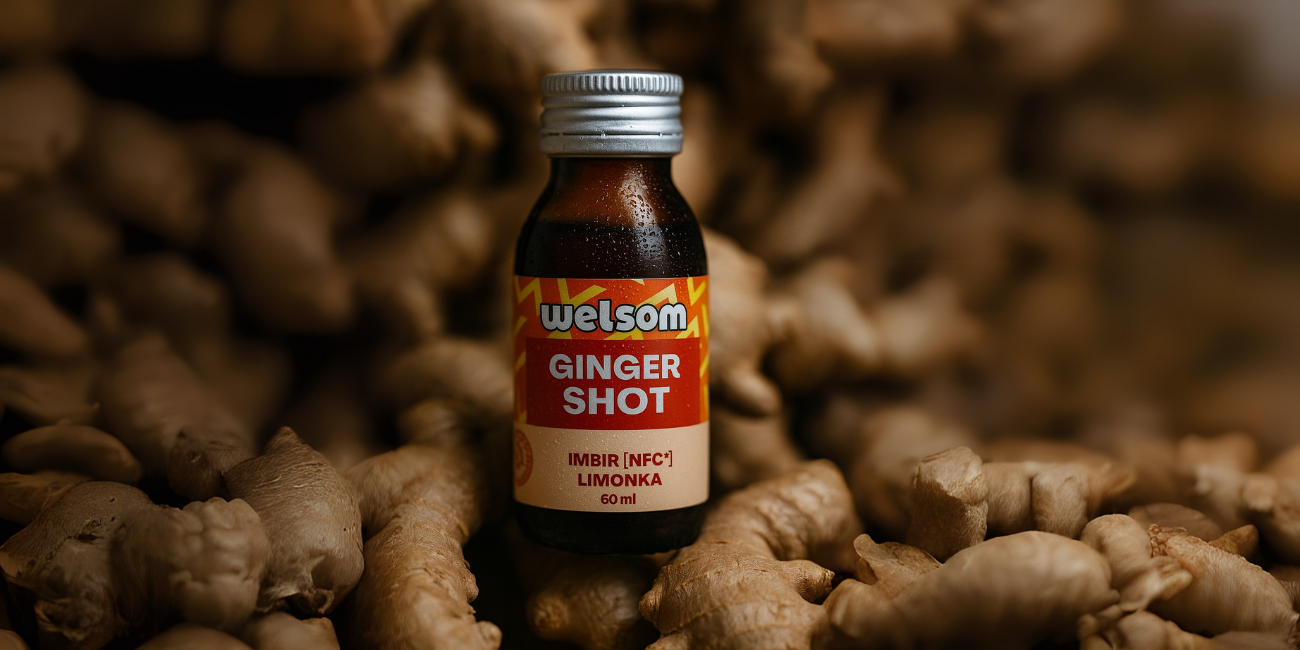 Butelka Ginger Shot Welsom stojąca pomiędzy kłączami imbiru.